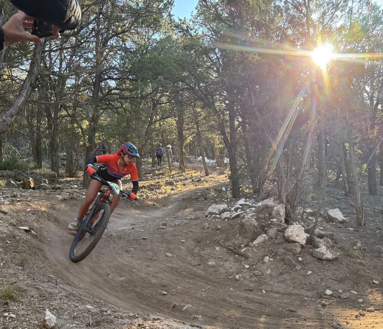 Racer rips through a bermed corner with a bright sun shining through the trees